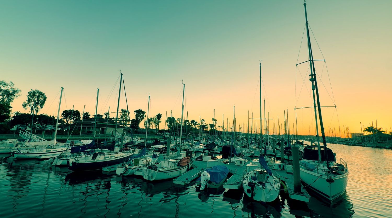 Panoramic view of sailboats moored at a marina during sunset with a teal-tinted sky.