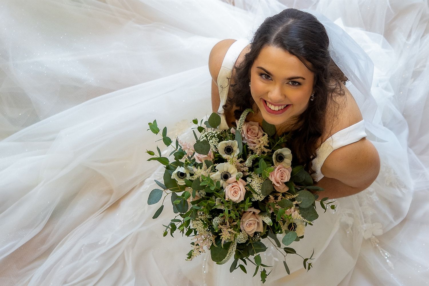 Wedding rings nestled among white roses and pearl-accented flowers in a bridal bouquet arrangement.