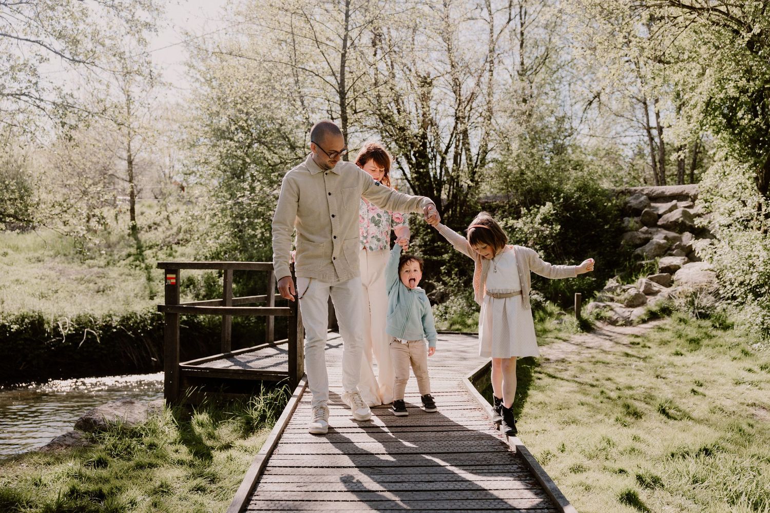Happy family of four walking together on a wooden bridge surrounded by lush green trees.