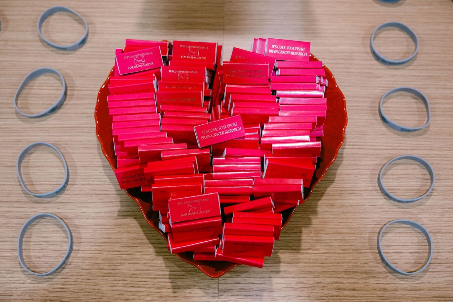 Red paper notes arranged in a heart shape pattern on a wooden surface with metallic rings in the background.