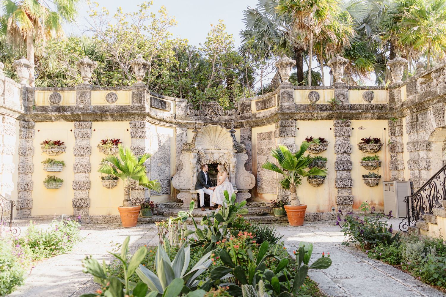 A series of elegant stone archways with tropical plants line a courtyard in a Mediterranean-style building.