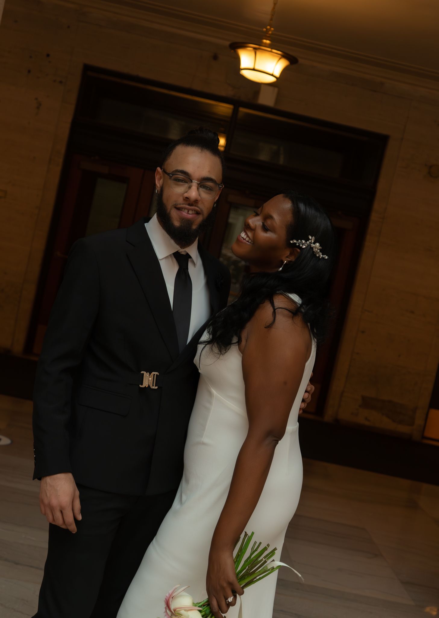 Bride and groom descend grand staircase in ornate hall, she in white gown, he in black suit.