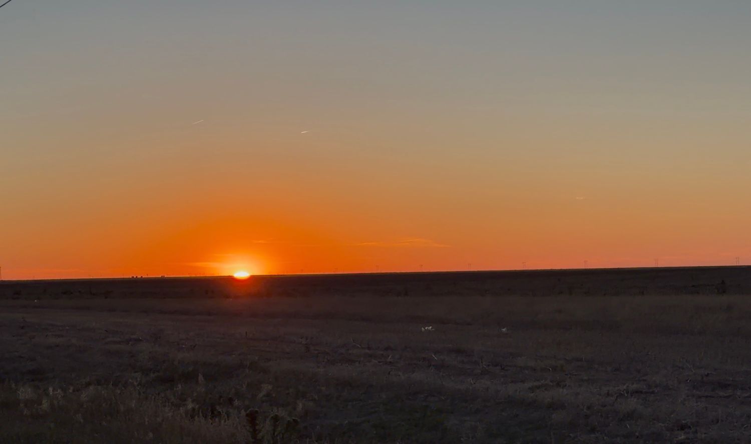 Vibrant orange sunset over flat prairie horizon with clear sky gradient from orange to blue.