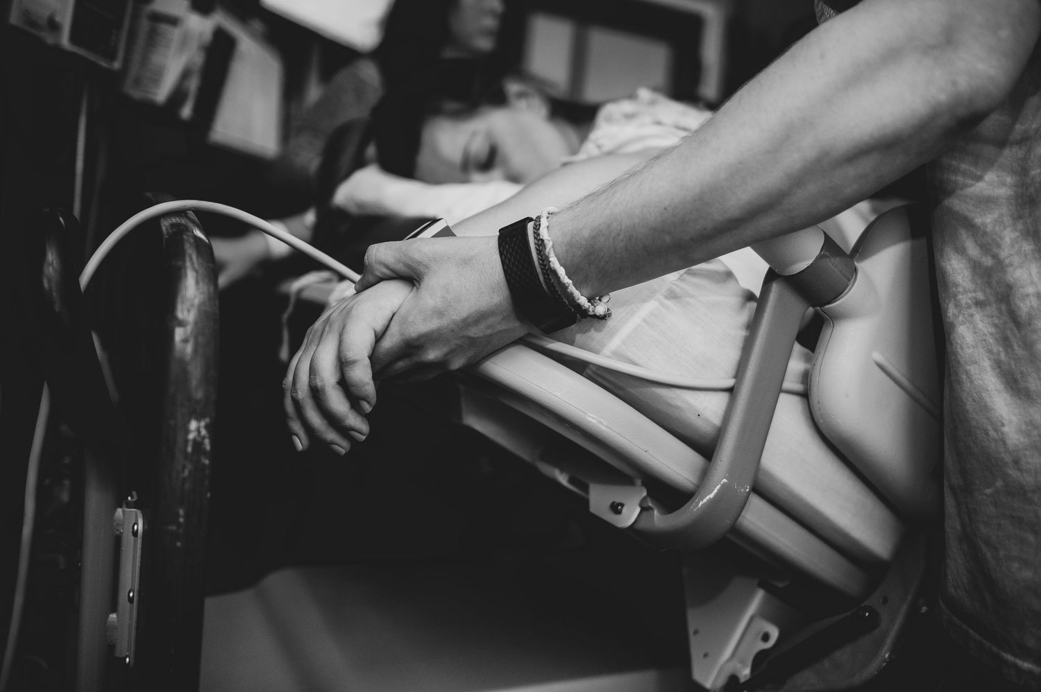 Black and white photo of hands gripping a chair rail, with a person in the background.