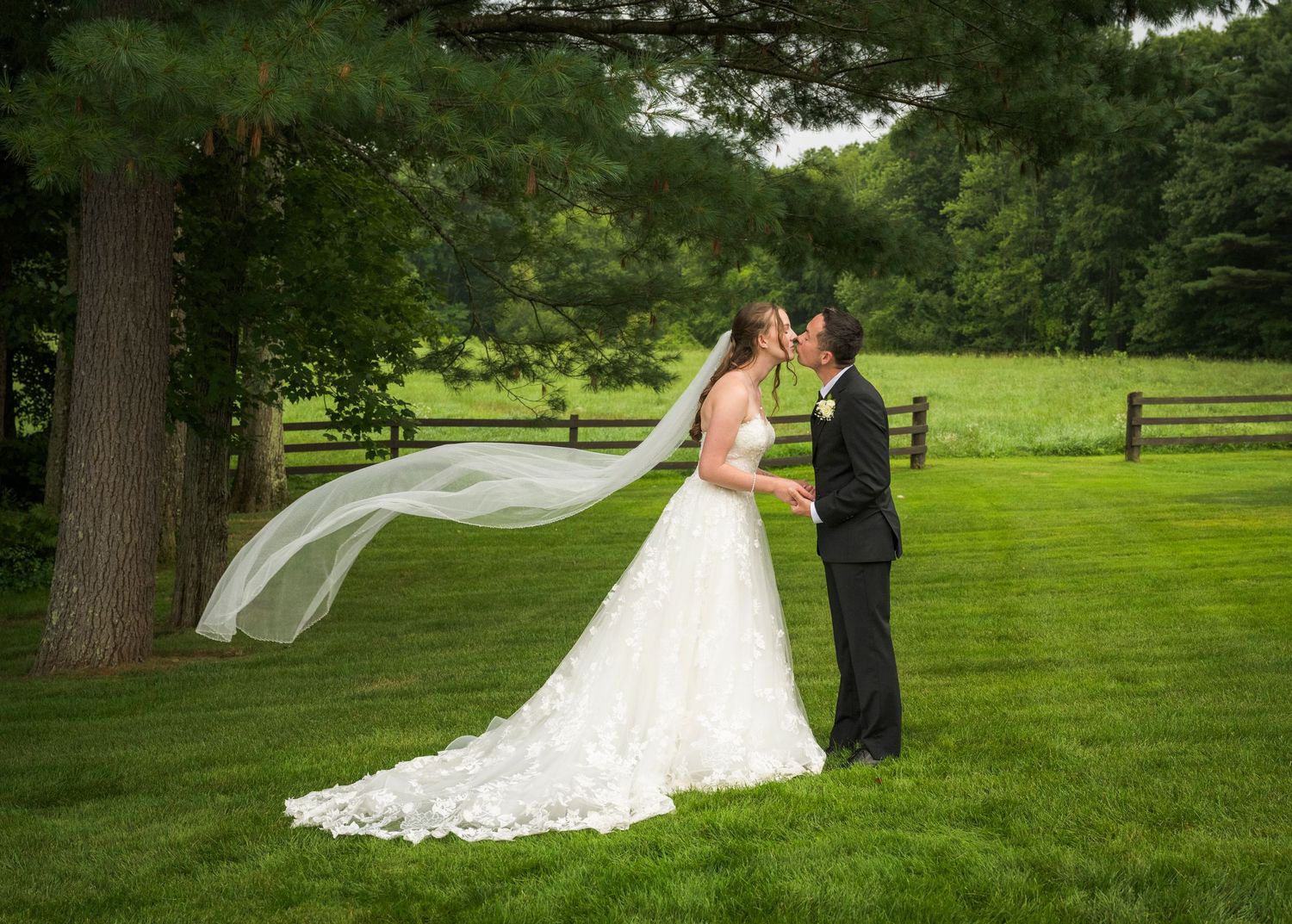 Newlyweds share an intimate moment outdoors with autumn foliage and rustic architecture in background.