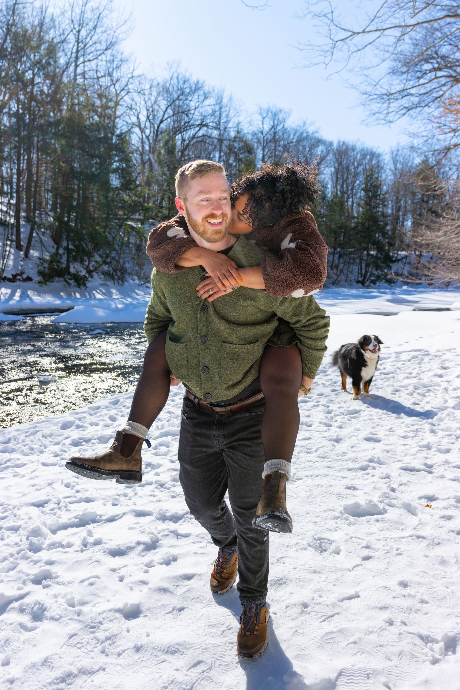 A couple shares an intimate moment together in a snowy winter setting wearing casual outdoor clothing.