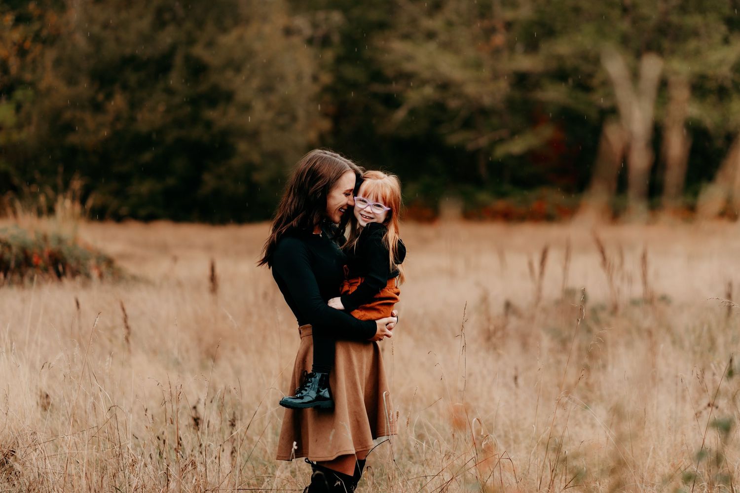 A mother holds her young daughter in a golden autumn field, sharing a tender embrace surrounded by fall foliage during fall photos in Tacoma