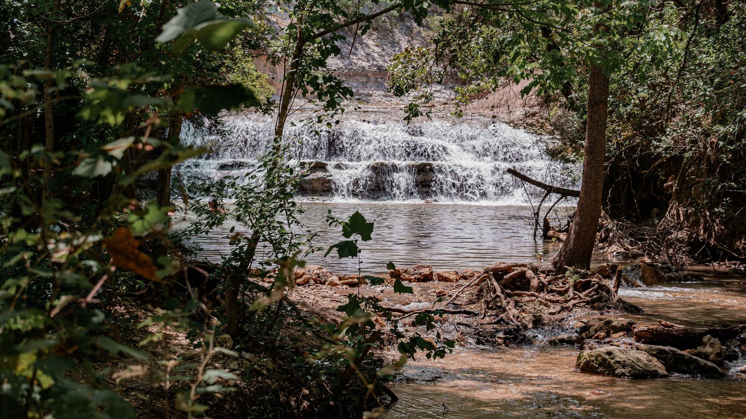 Lush tropical waterfall cascading over rocky tiers into a serene pool, surrounded by dense green forest trees.