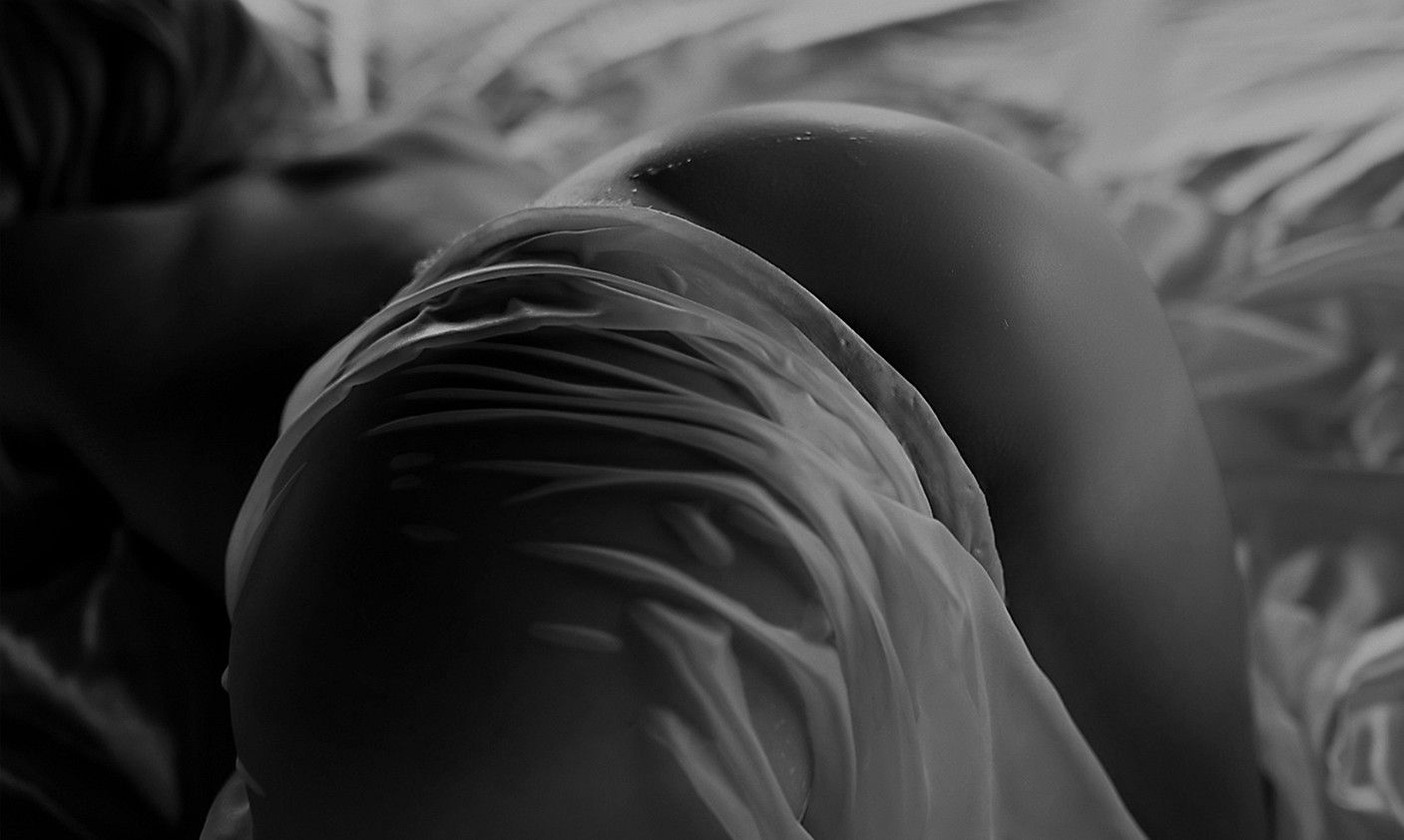 Black and white artistic photo of a figure draped in soft fabric, creating elegant curves and shadows.