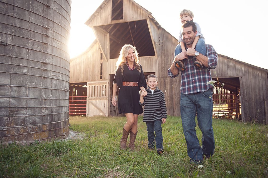 Family of four walking near rustic barn and silo on a farm at golden hour sunset.