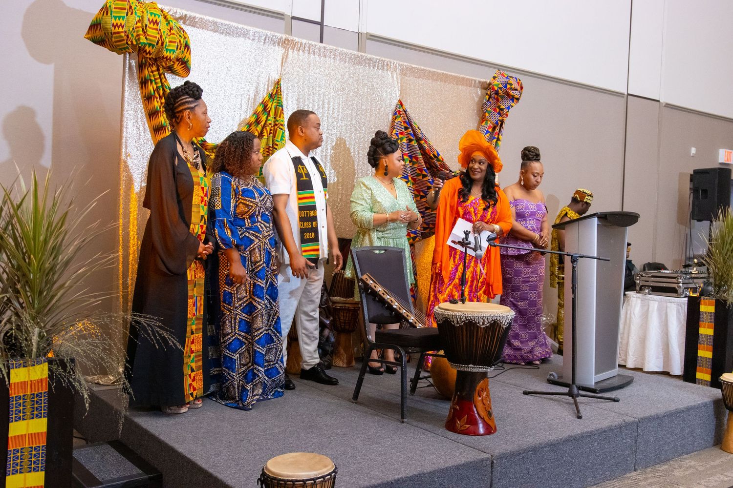 Diverse guests in colorful African attire attend a formal banquet event with a speaker at the podium.