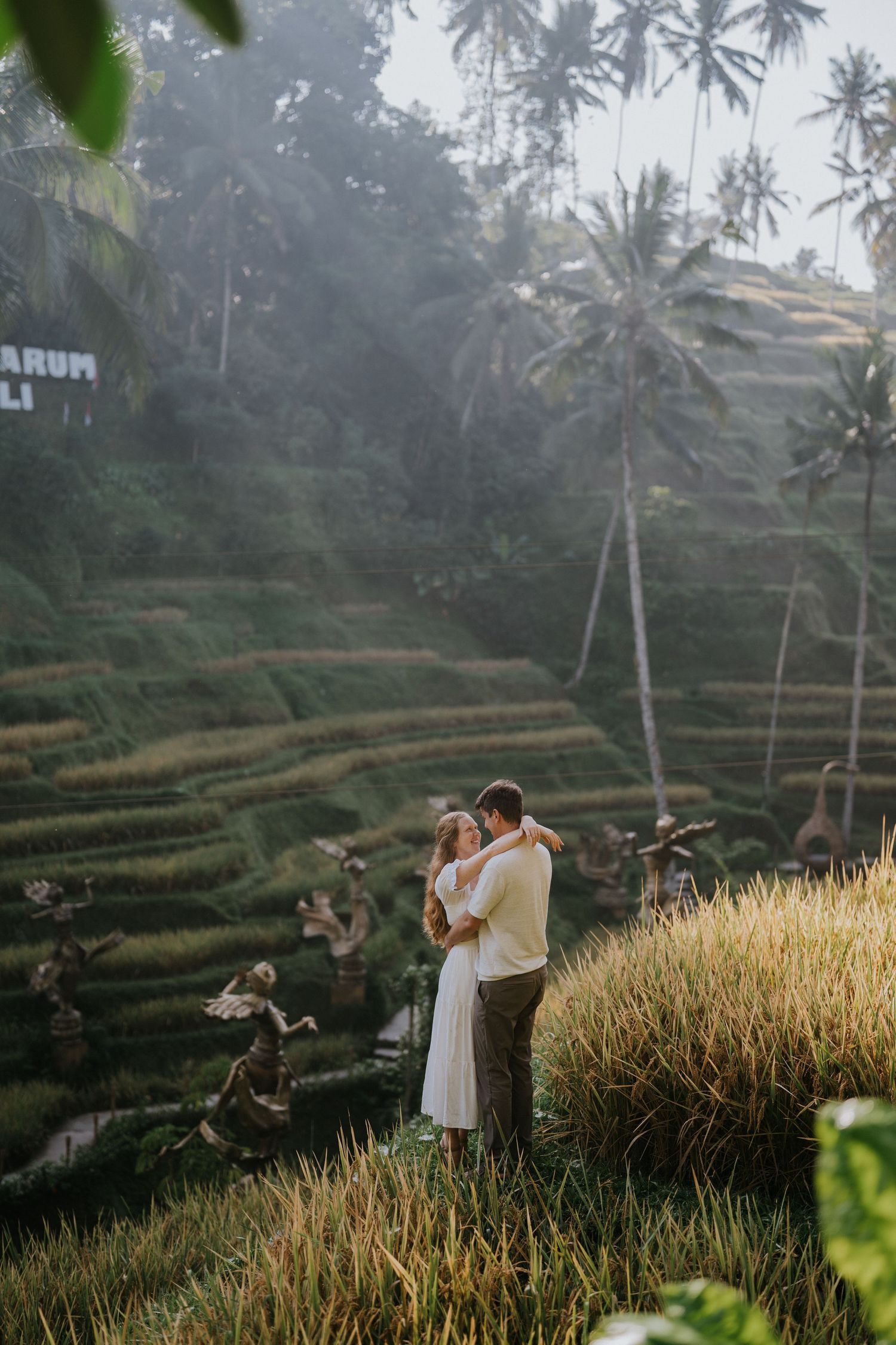 A couple poses on a rope bridge surrounded by tropical vegetation.