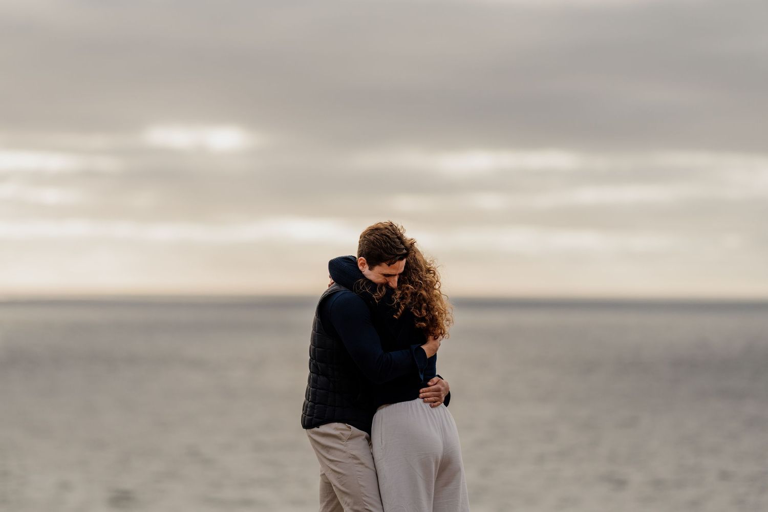 couple hugging after proposal on trevose head in cornwall during golden hour