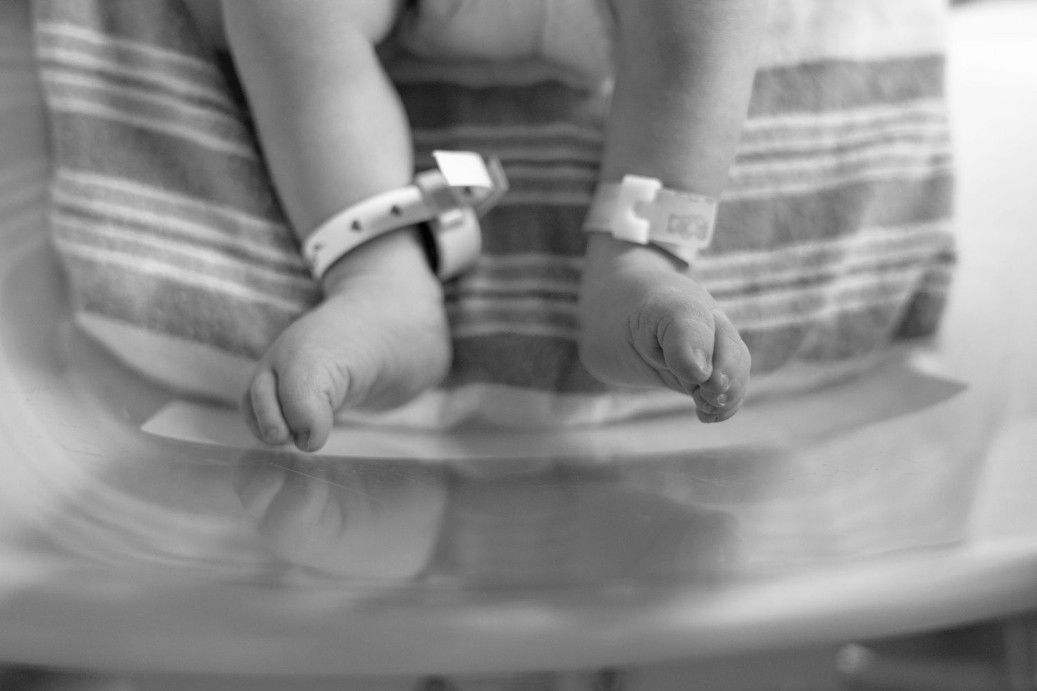 Black and white photo of newborn baby feet with hospital ID bracelets in a bassinet.