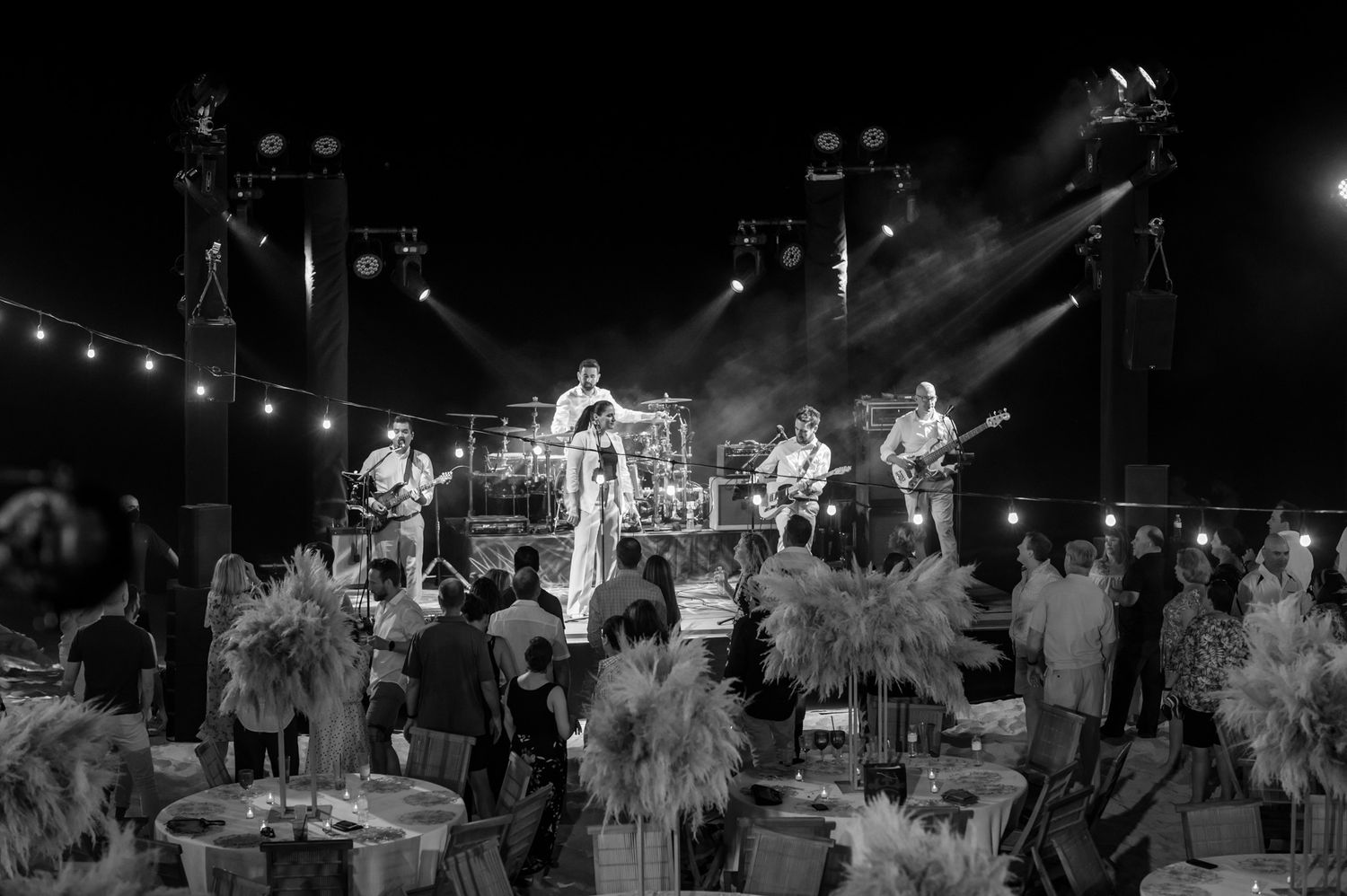 Live band performs on a dramatic stage with purple lights and fog at an elegant outdoor wedding reception.