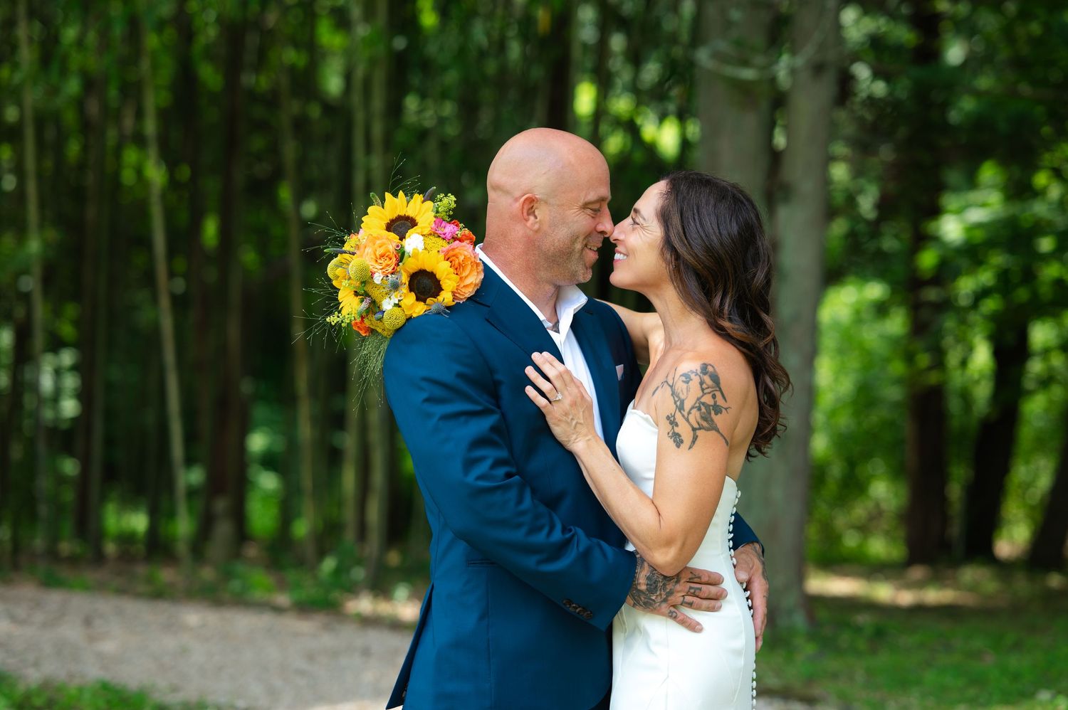 Bride and groom share a romantic moment outdoors, with sunflower bouquet, lush green trees at the Hammond Museum & Japanese Stroll Gardens.
