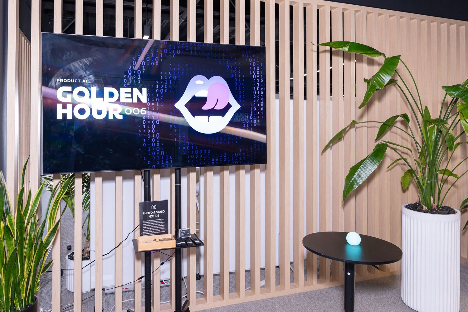 A Golden Hour event display screen on a stand in a modern lounge with green plants and sleek wood panel walls.