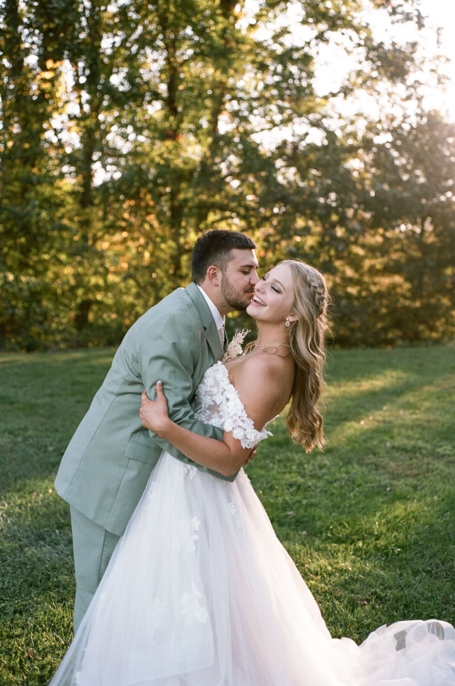 Newlywed couple embraces in a romantic outdoor wedding photo with golden sunlight filtering through autumn trees.