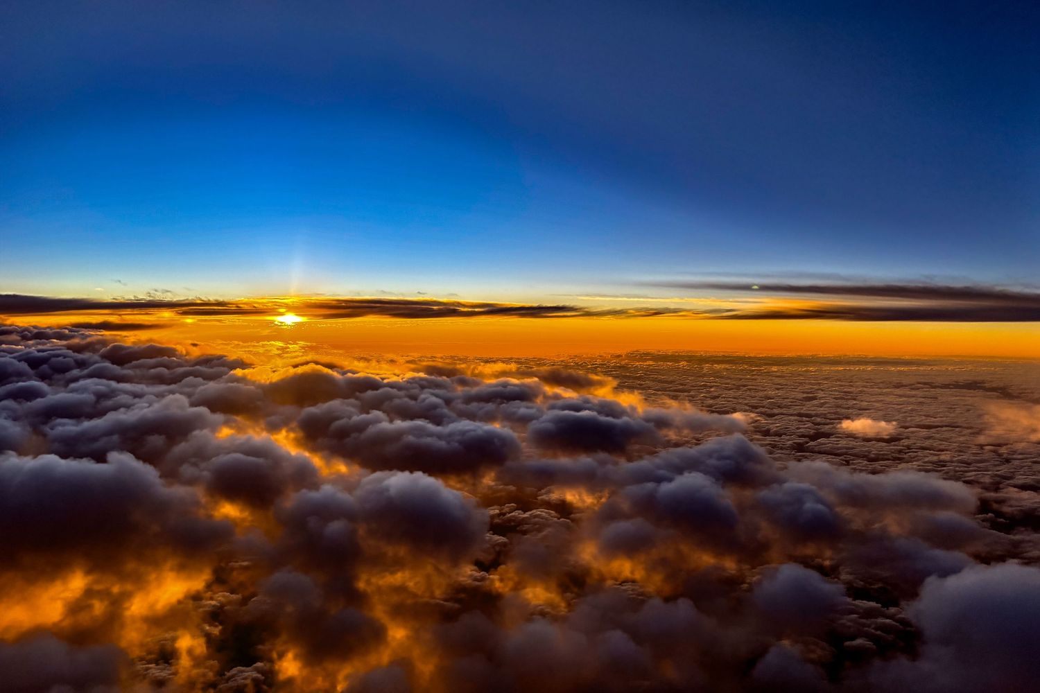Dramatic sunset above clouds with orange and purple hues painting the sky.