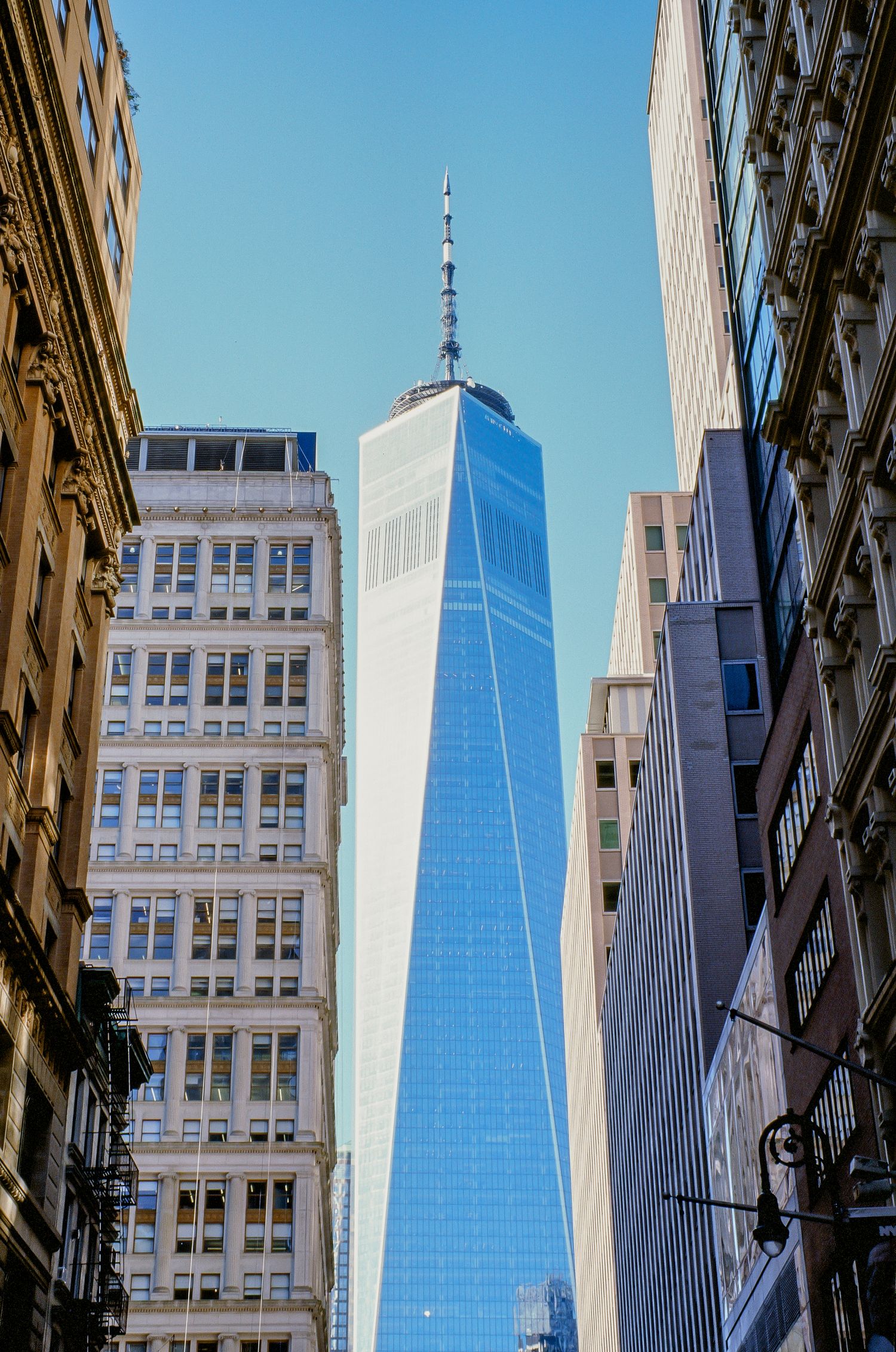 One World Trade Center tower photographed from street level against blue sky in Manhattan.