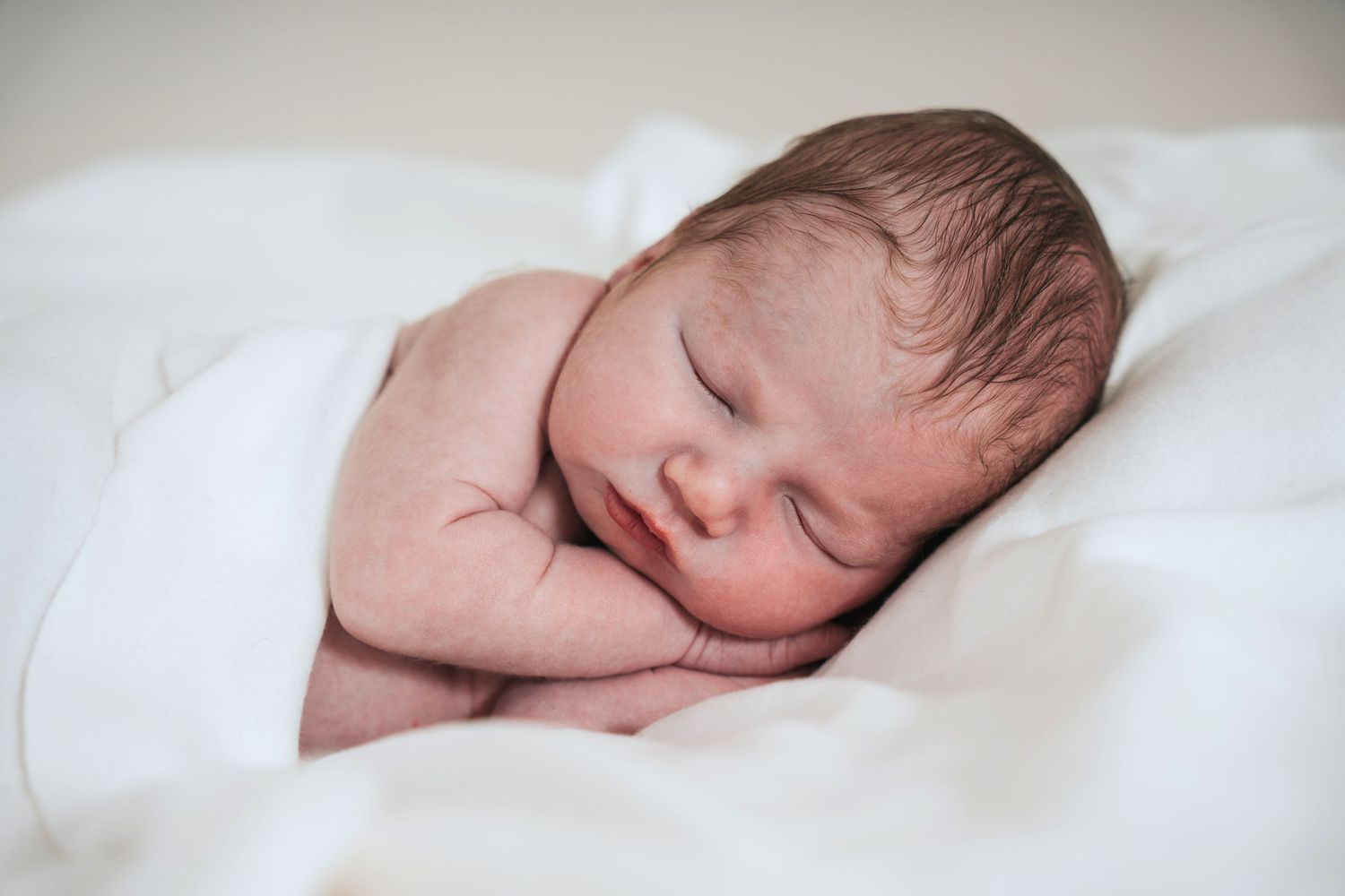 Devon newborn baby photographer takes close up of sleeping baby with hands under his face.