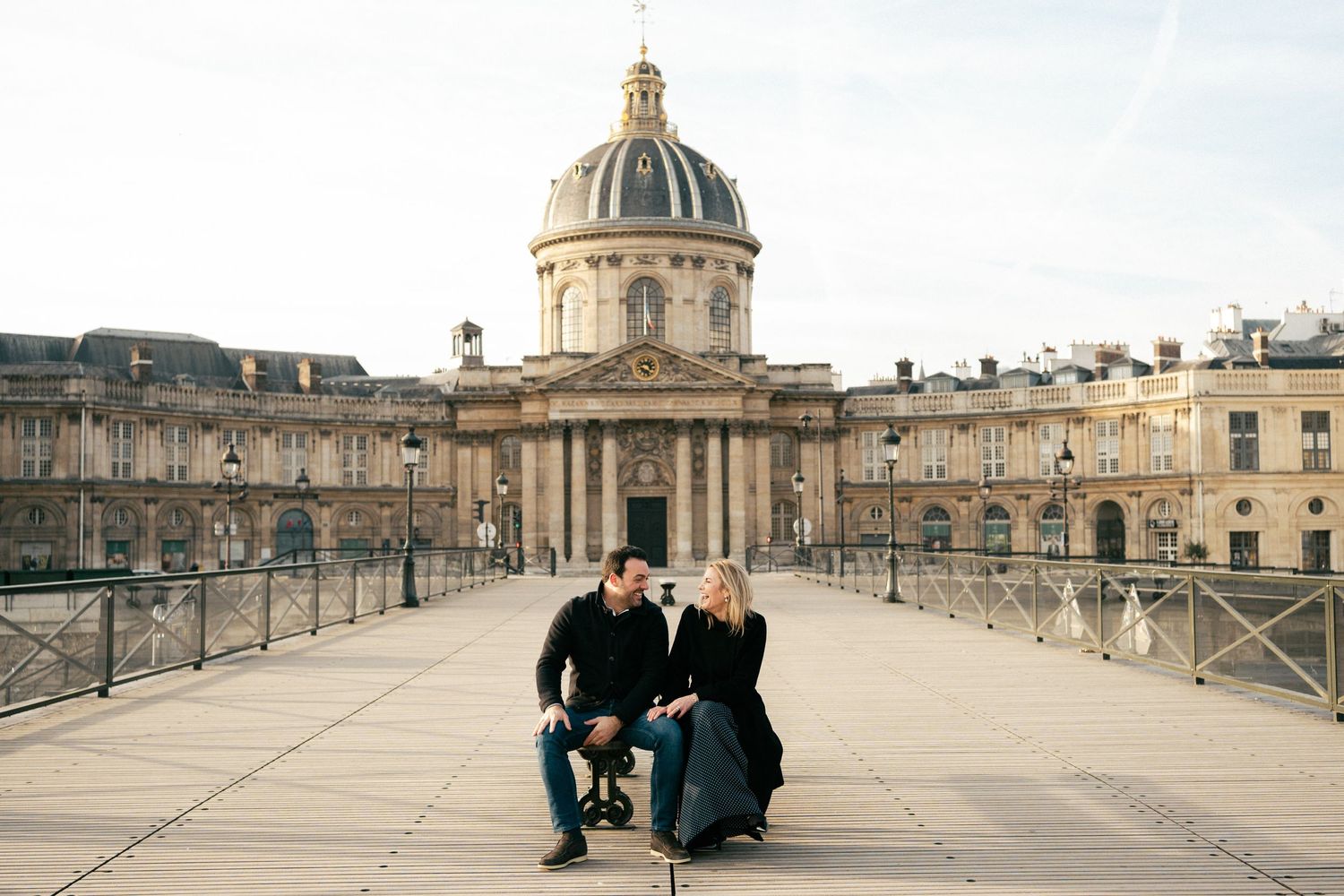 A couple sits together on the Pont des Arts bridge with the Institut de France dome in the background in Paris.