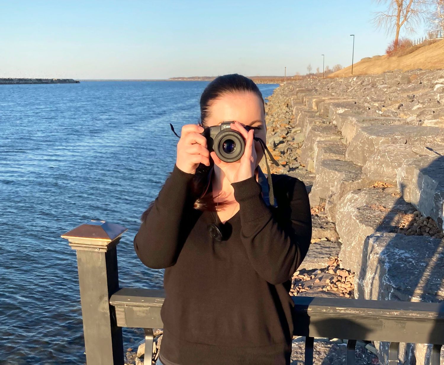 Woman stood next to a body of water, holding a camera up to her face - Parker photographer