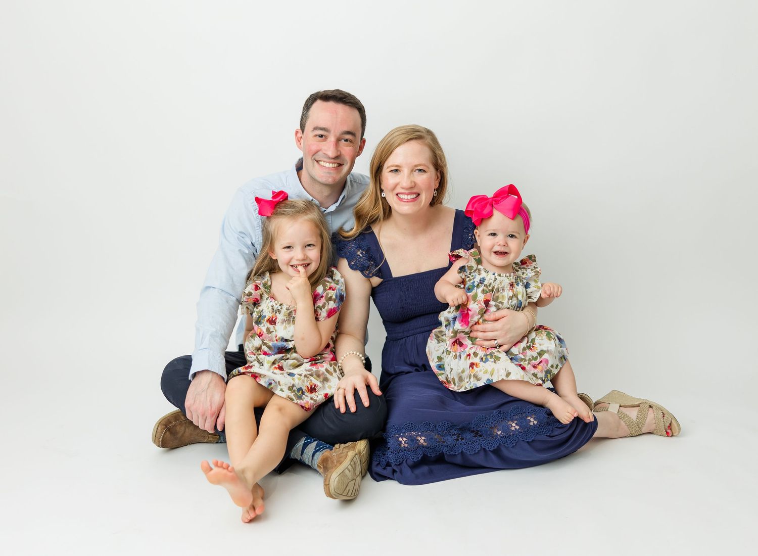Family portrait with parents and two children wearing coordinated floral outfits against white background.
