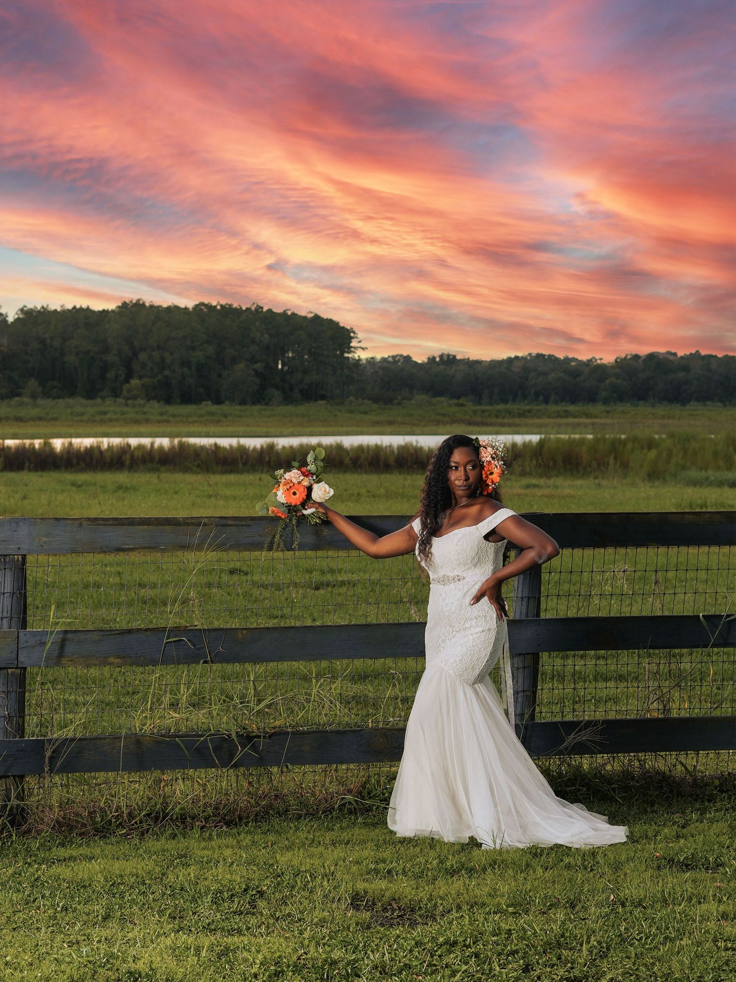 Dramatic sunset wedding photo with white gown and peach bouquet against rural landscape.