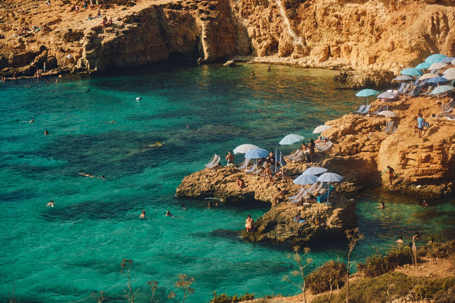 Crystal clear turquoise waters meet rocky cliffs in a Mediterranean cove.