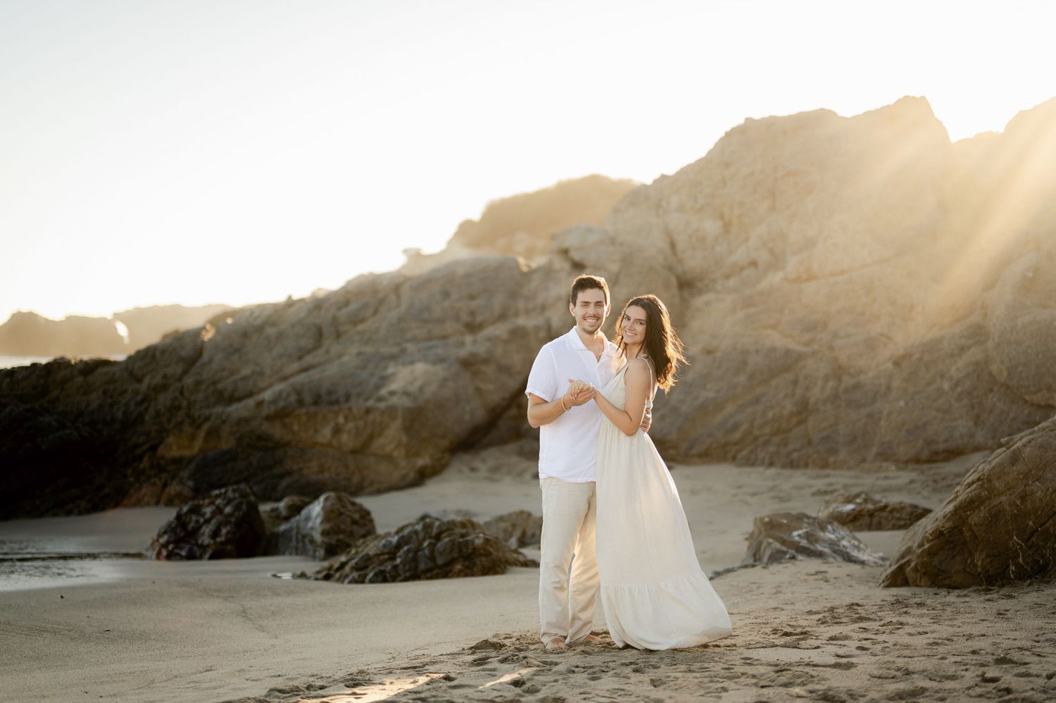 A romantic sunset moment on a beach with rocky cliffs in the background.