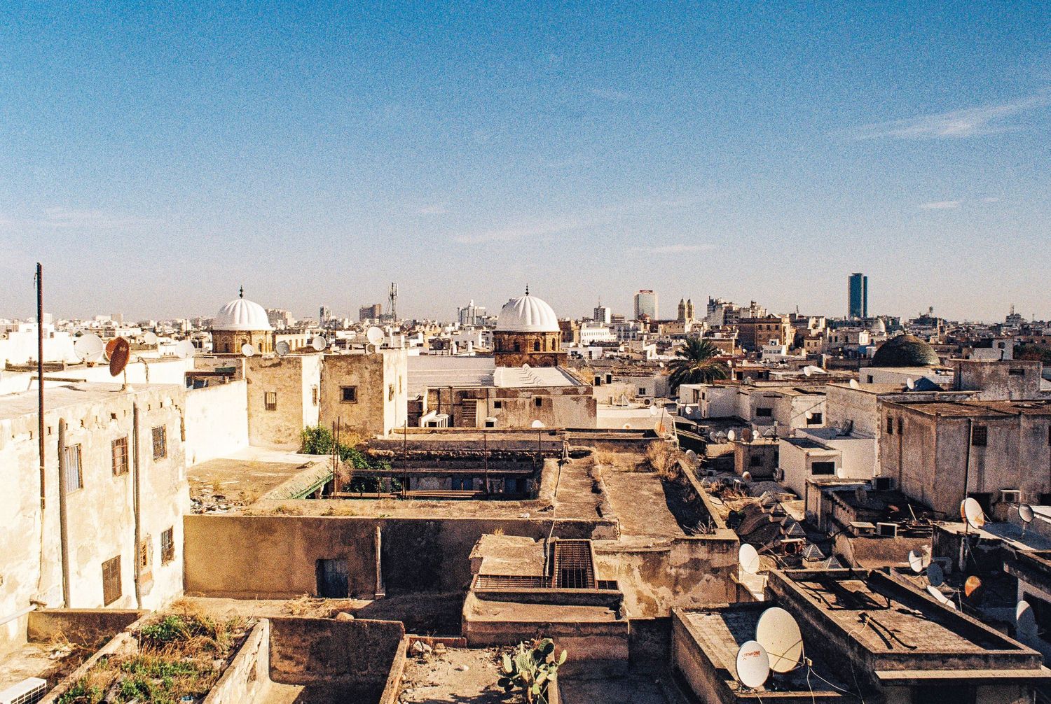 Urban rooftop view across Medina with traditional North African architecture and satellite dishes against blue sky.