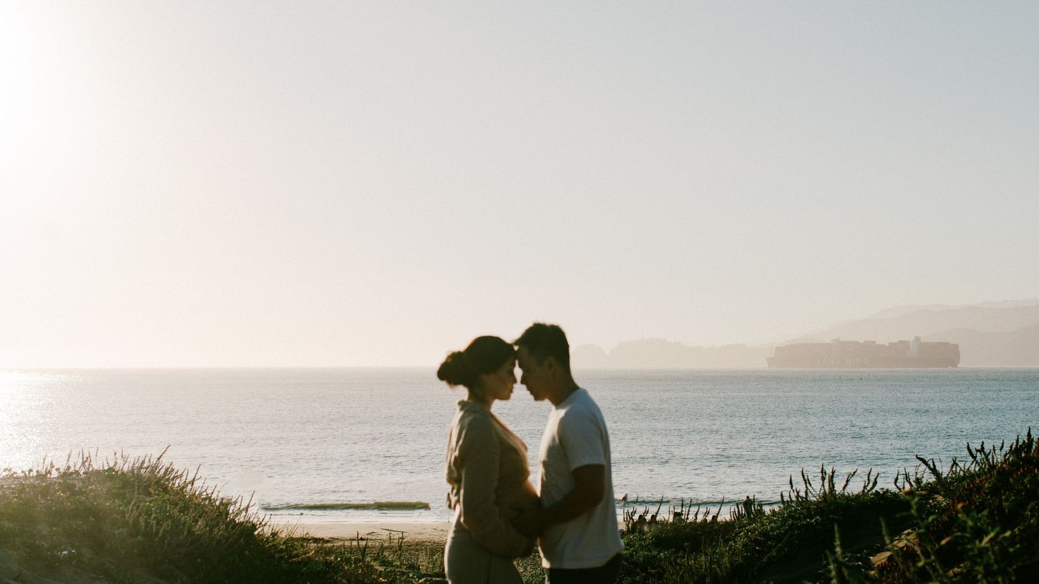 Silhouetted couple sharing tender moment against ocean backdrop at dusk.