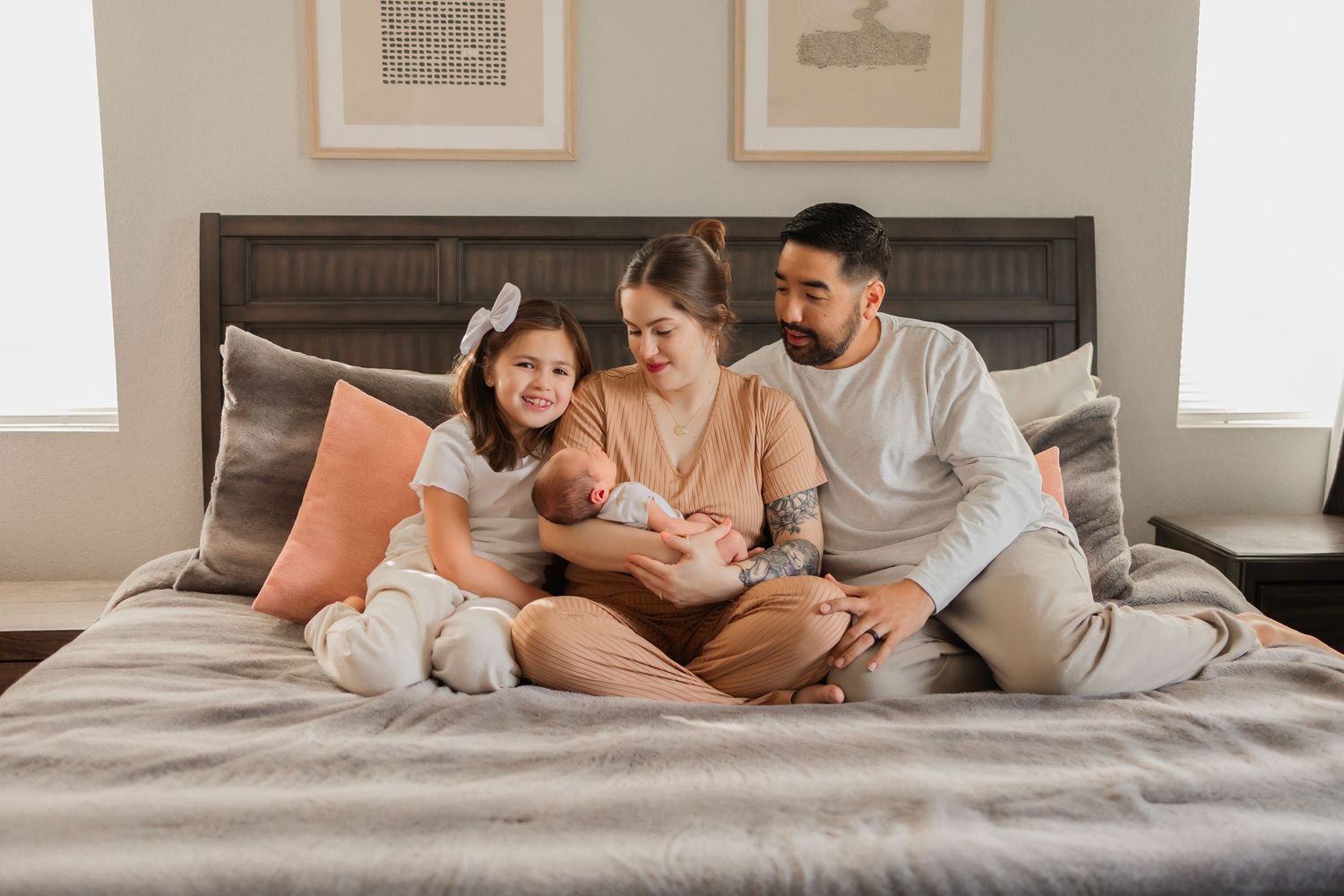 A heartfelt family portrait on a softly lit bed, with parents and a proud big sister adoring their newborn baby.