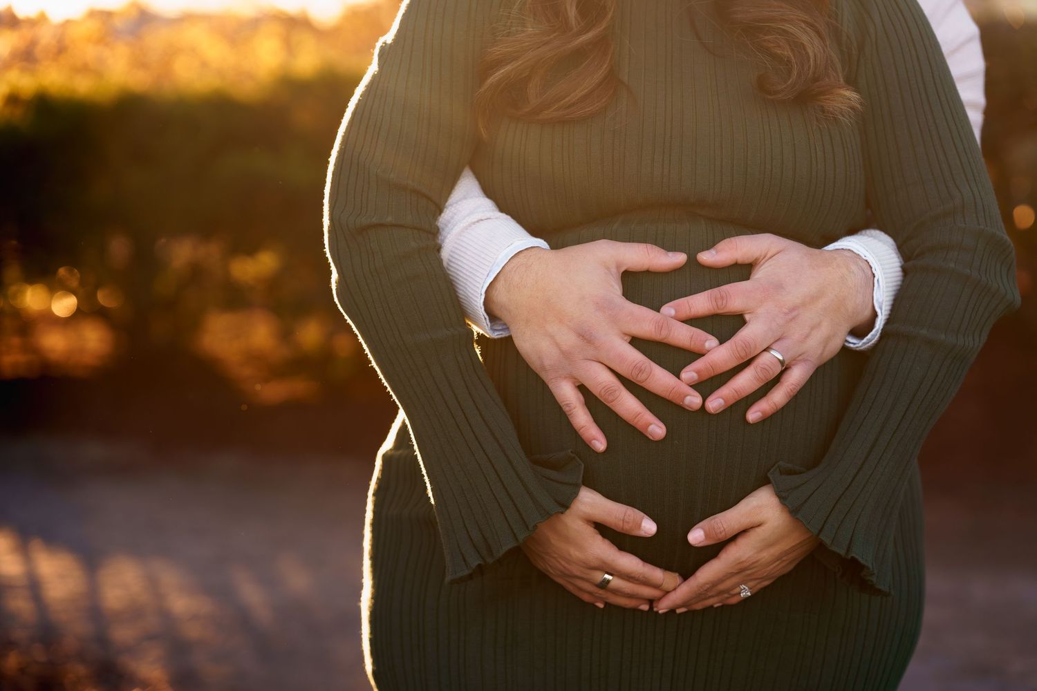 Close-up of pregnant belly with tiny white baby booties resting on top against dark background, home session in Frederick Maryland