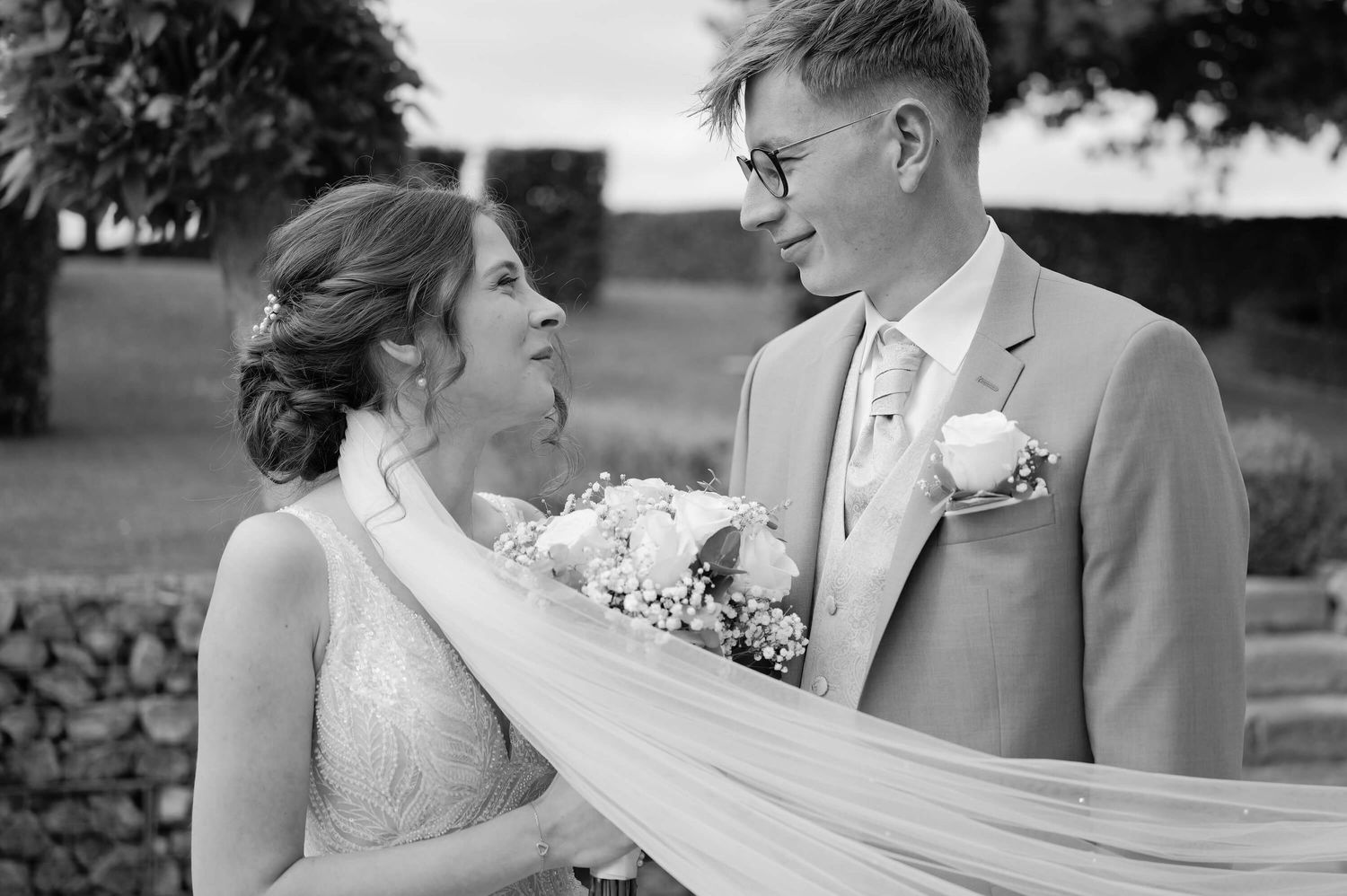 A black and white wedding photo showing a joyful moment between newlyweds with the bride wearing a flowing veil.