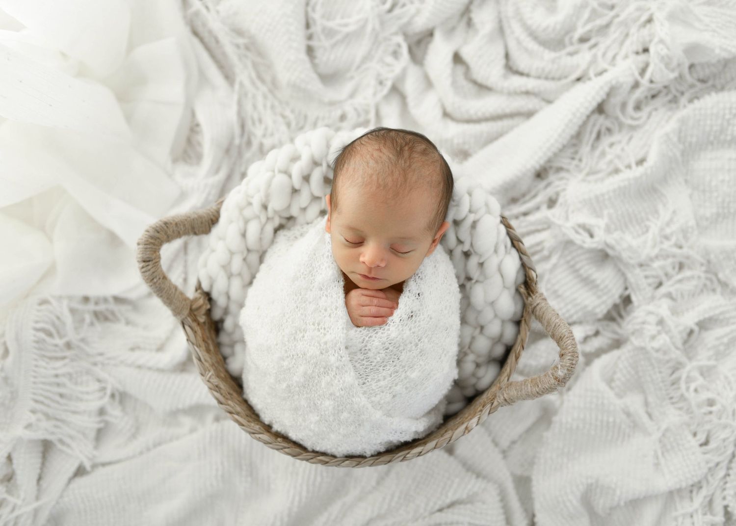 Sleeping newborn wrapped in white lace fabric with soft natural lighting.