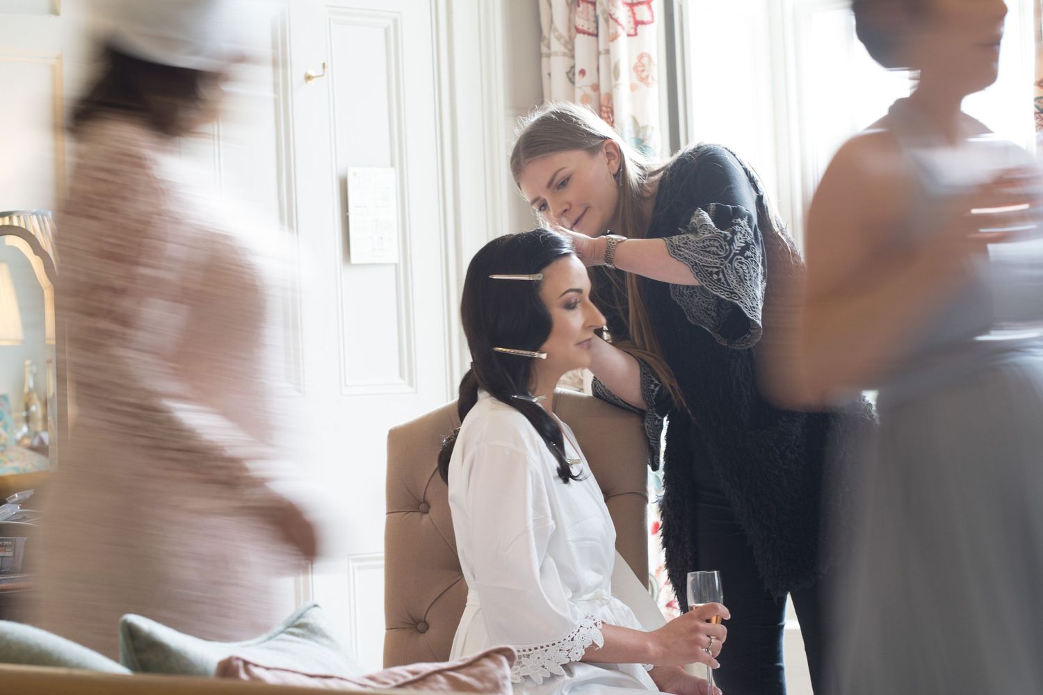 A blurred scene shows several people in motion during wedding preparations, at Westin Hotel, Halifax with bride seated wearing a white robe.