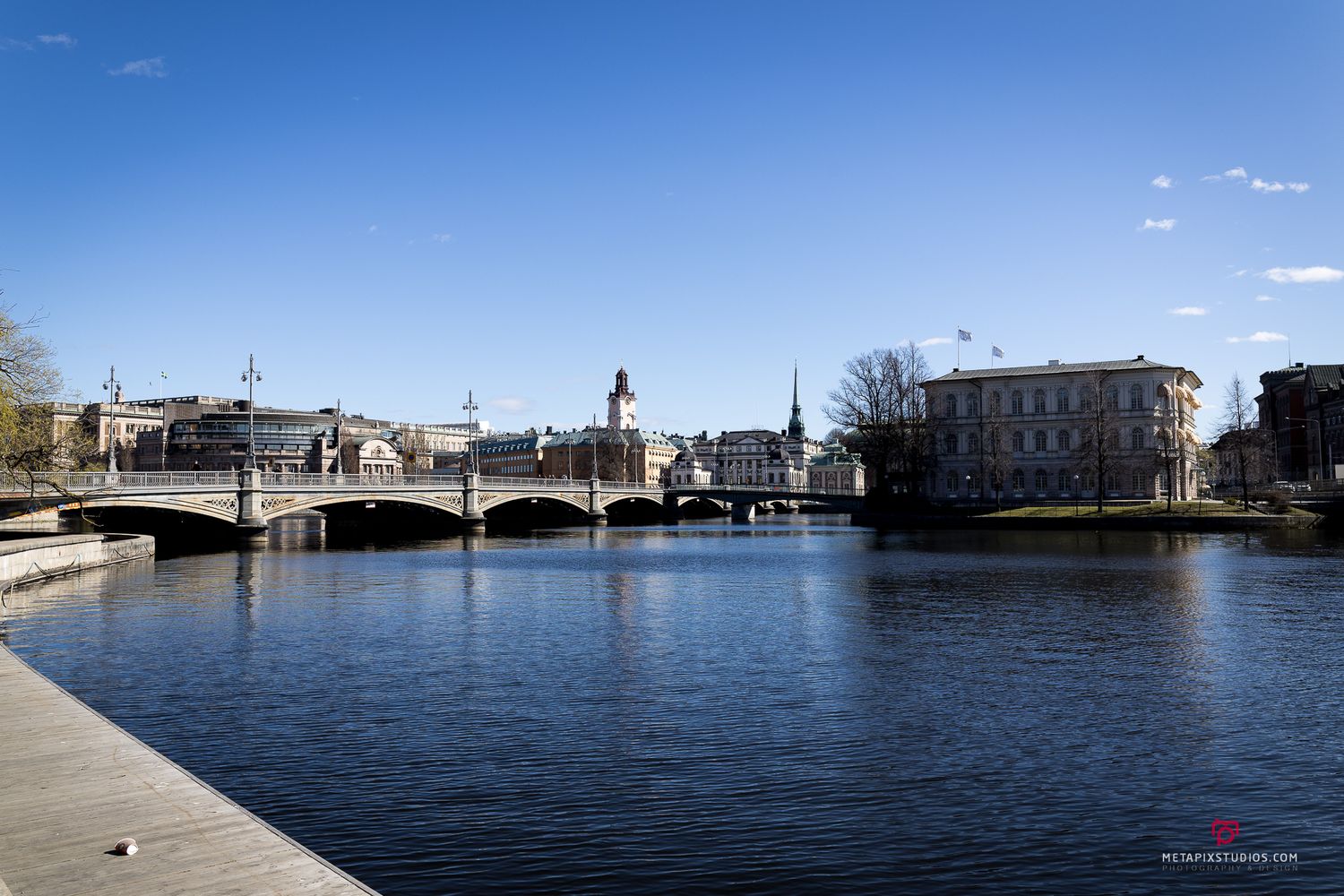 Scenic view of a stone bridge spanning a calm river in Sundsvall, Sweden, on a clear spring day.
