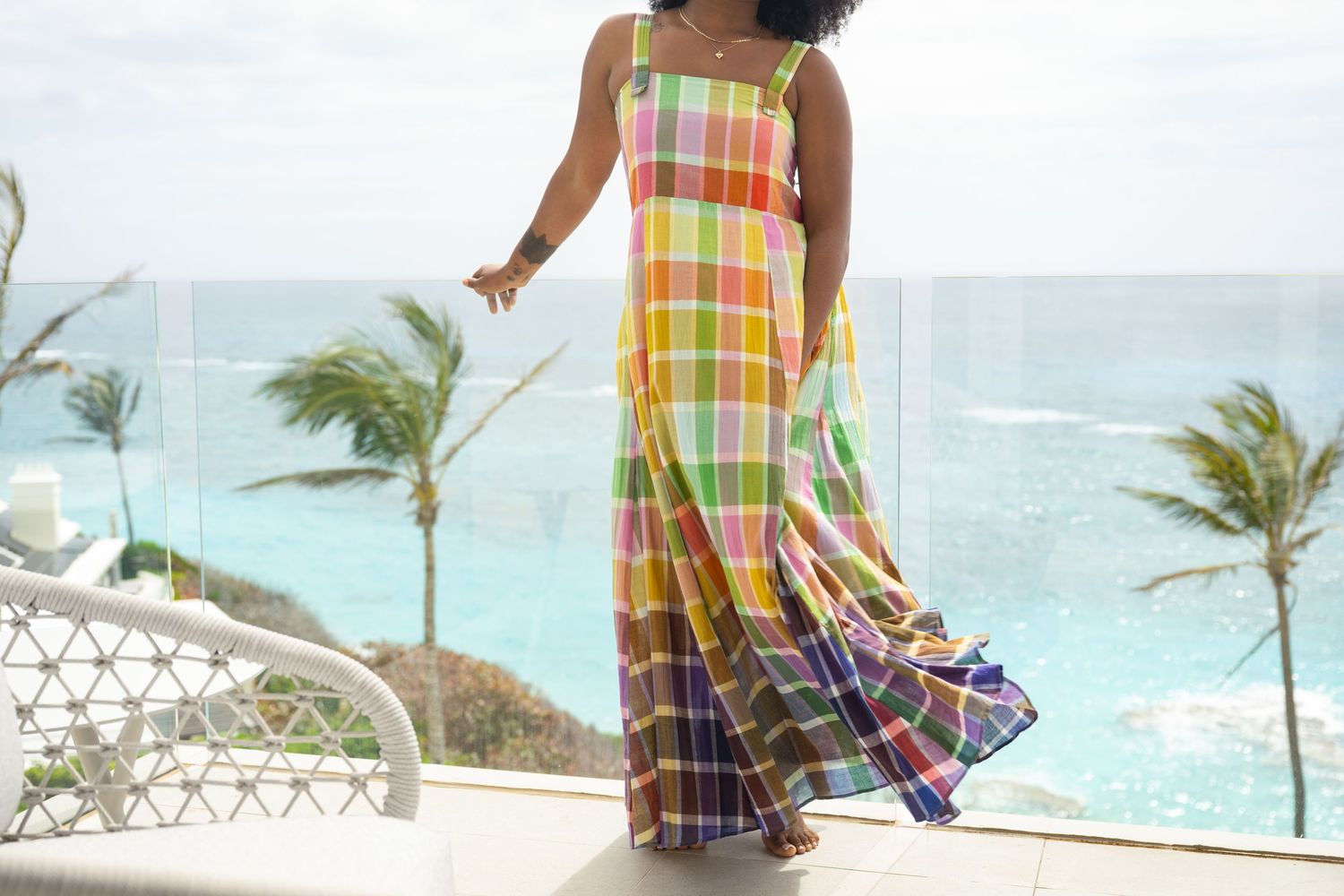 Flowing plaid maxi dress catching breeze against tropical oceanfront backdrop.