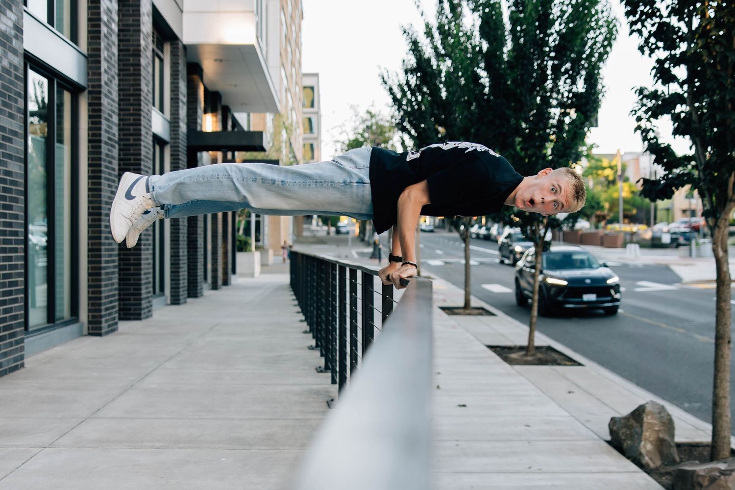 Athletic man performing a horizontal bar hold parkour move on a city railing outdoors.