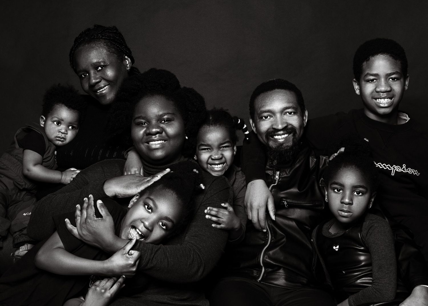Beautiful black and white portrait shows a joyful family with parents and children posing together against dark background.