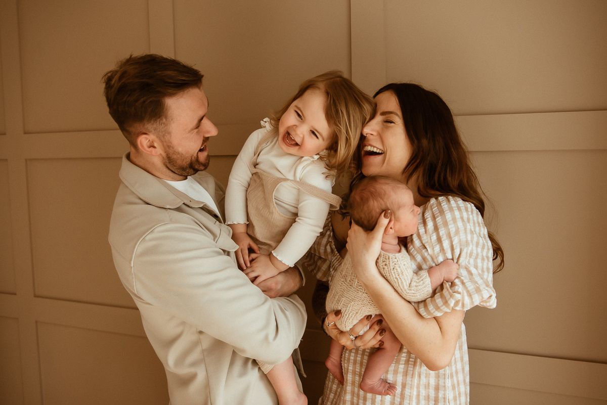A family shares a warm, joyful moment together laughing and embracing against a beige wall background.