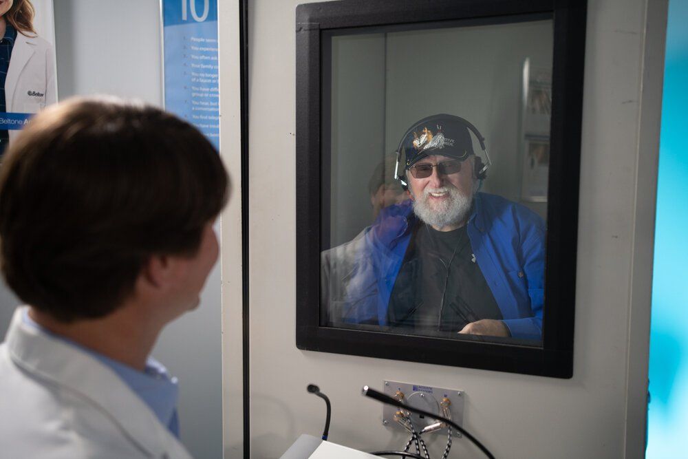 A medical consultation taking place through a glass window in a clinical setting.