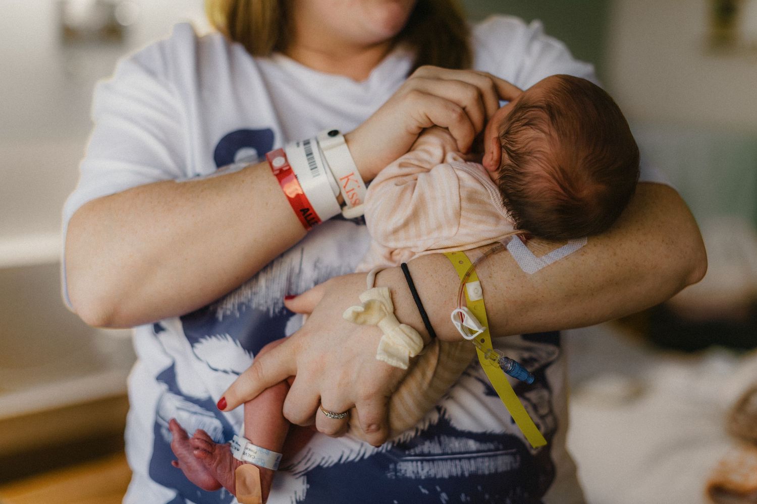 Close-up of caregiver holding and feeding newborn baby in hospital setting.