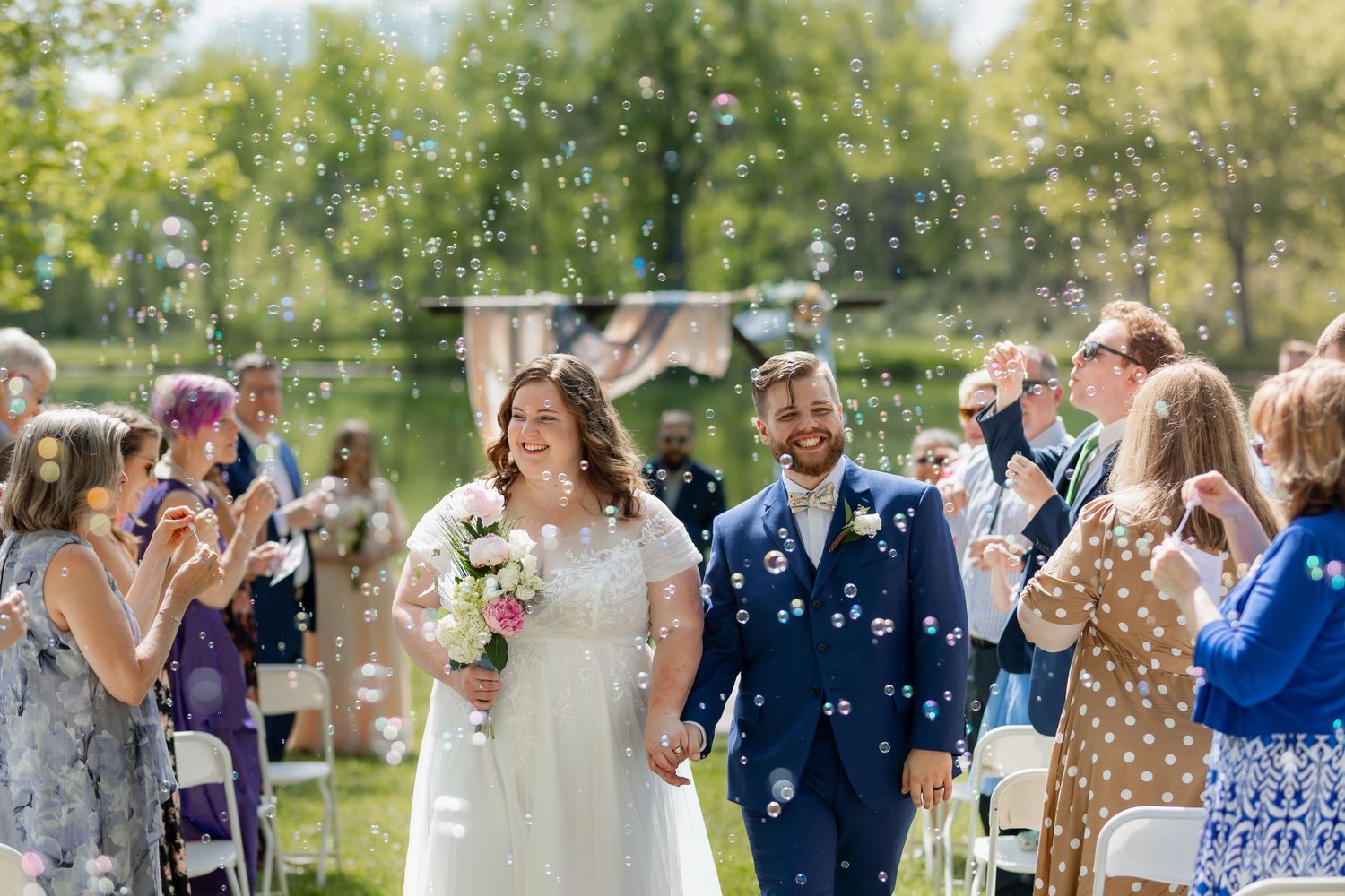 Joyful wedding celebration with bubbles floating through the air during outdoor ceremony.