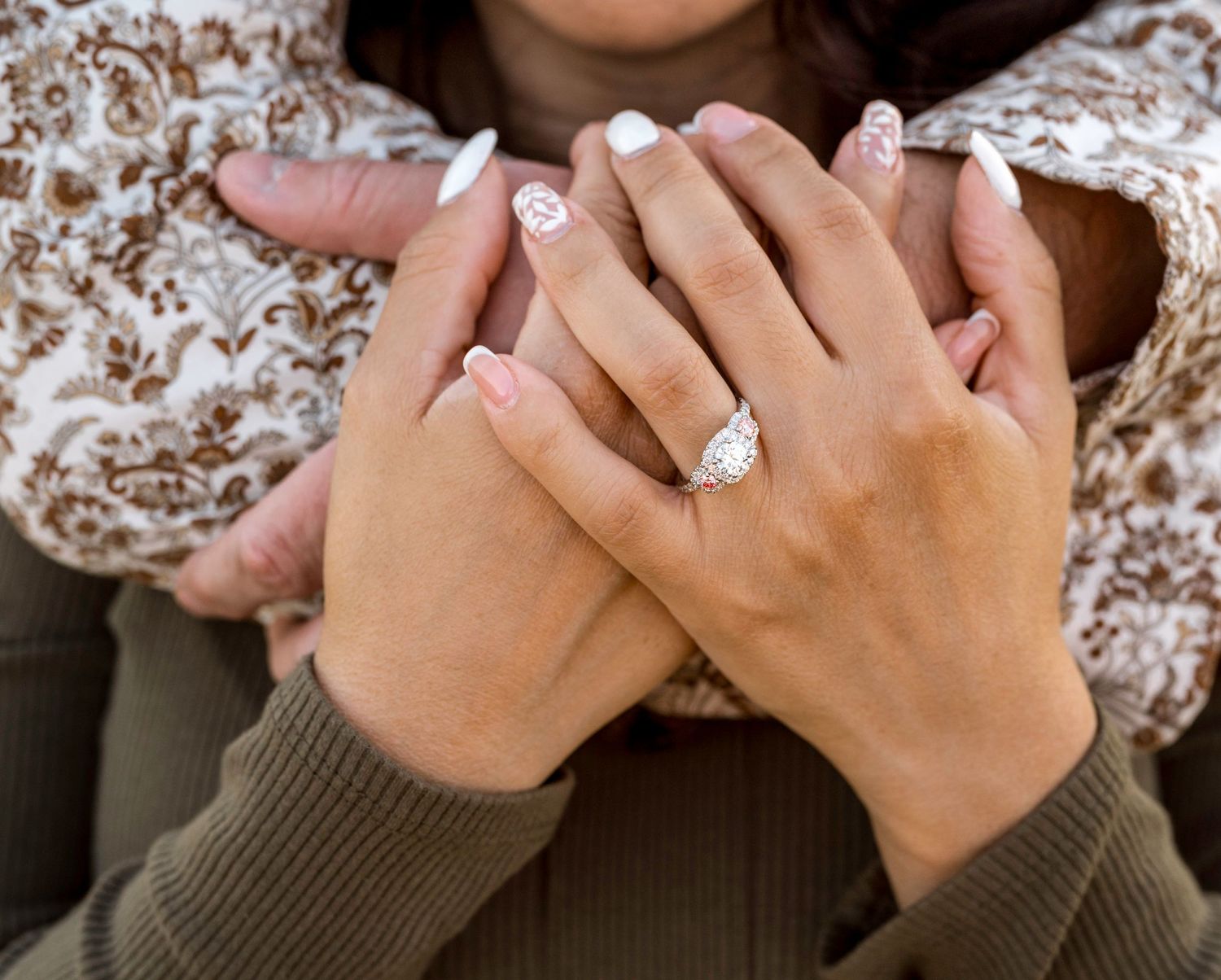 Close up of hands showing off engagement ring with delicate white manicure.