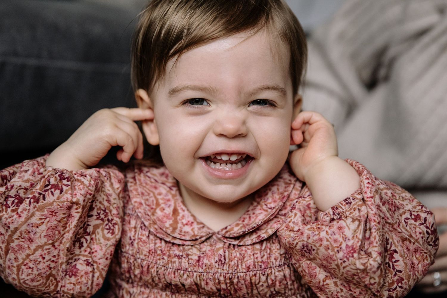 Joyful expression while wearing a pink smocked dress and playing with ears.