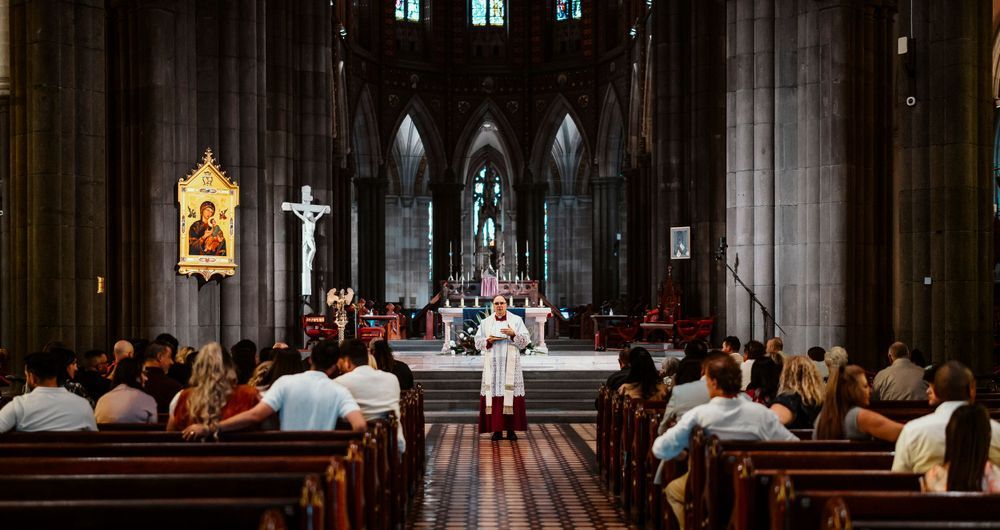 Catholic Mass ceremony inside a grand Gothic cathedral with congregation seated in wooden pews facing the altar.