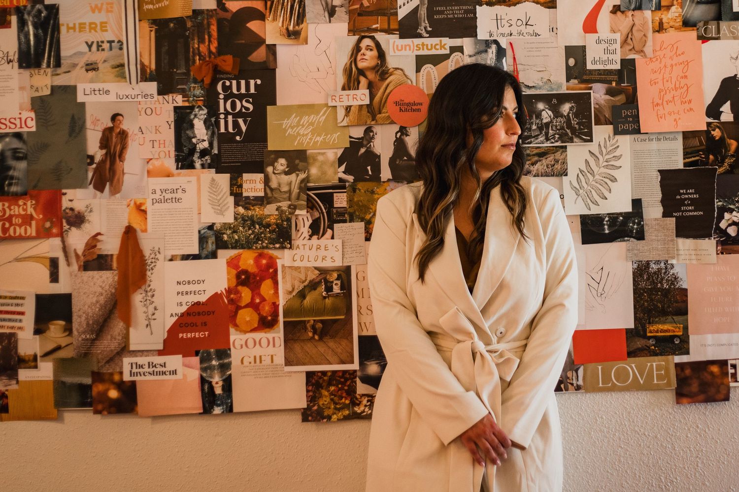 A person in a white robe standing against a wall covered with artistic vision board photos.